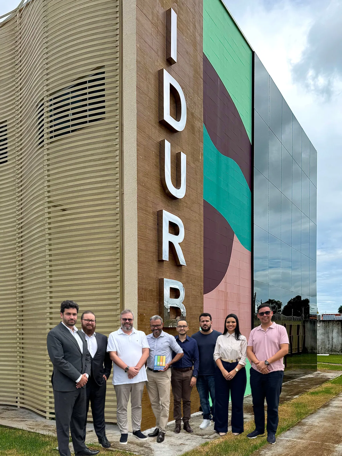 Equipe do projeto em frente à sede do IDURB, prédio com letreiro vertical, em Canaã dos Carajás